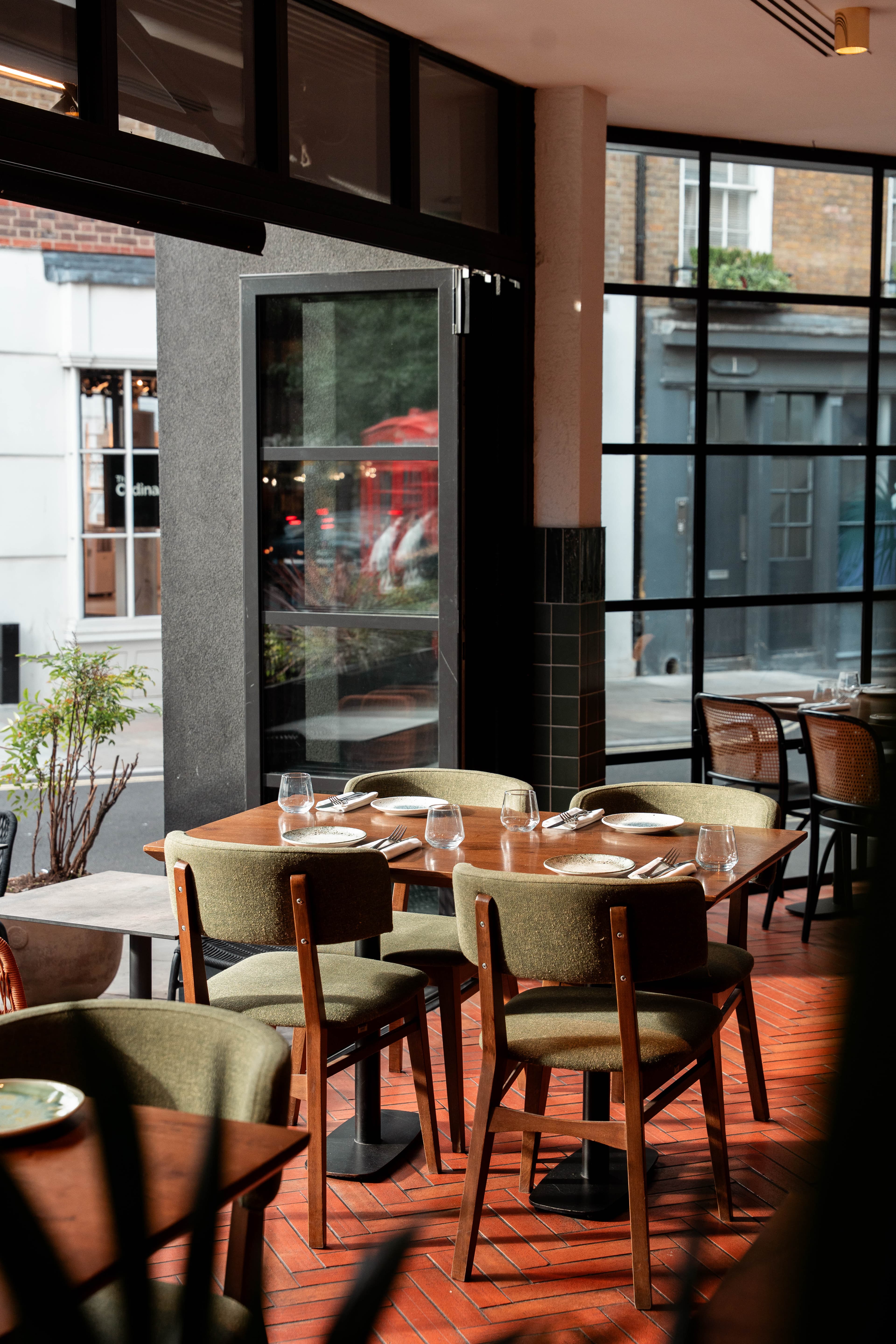 Sunlit tables set for guests beside Olea Social's street-facing windows