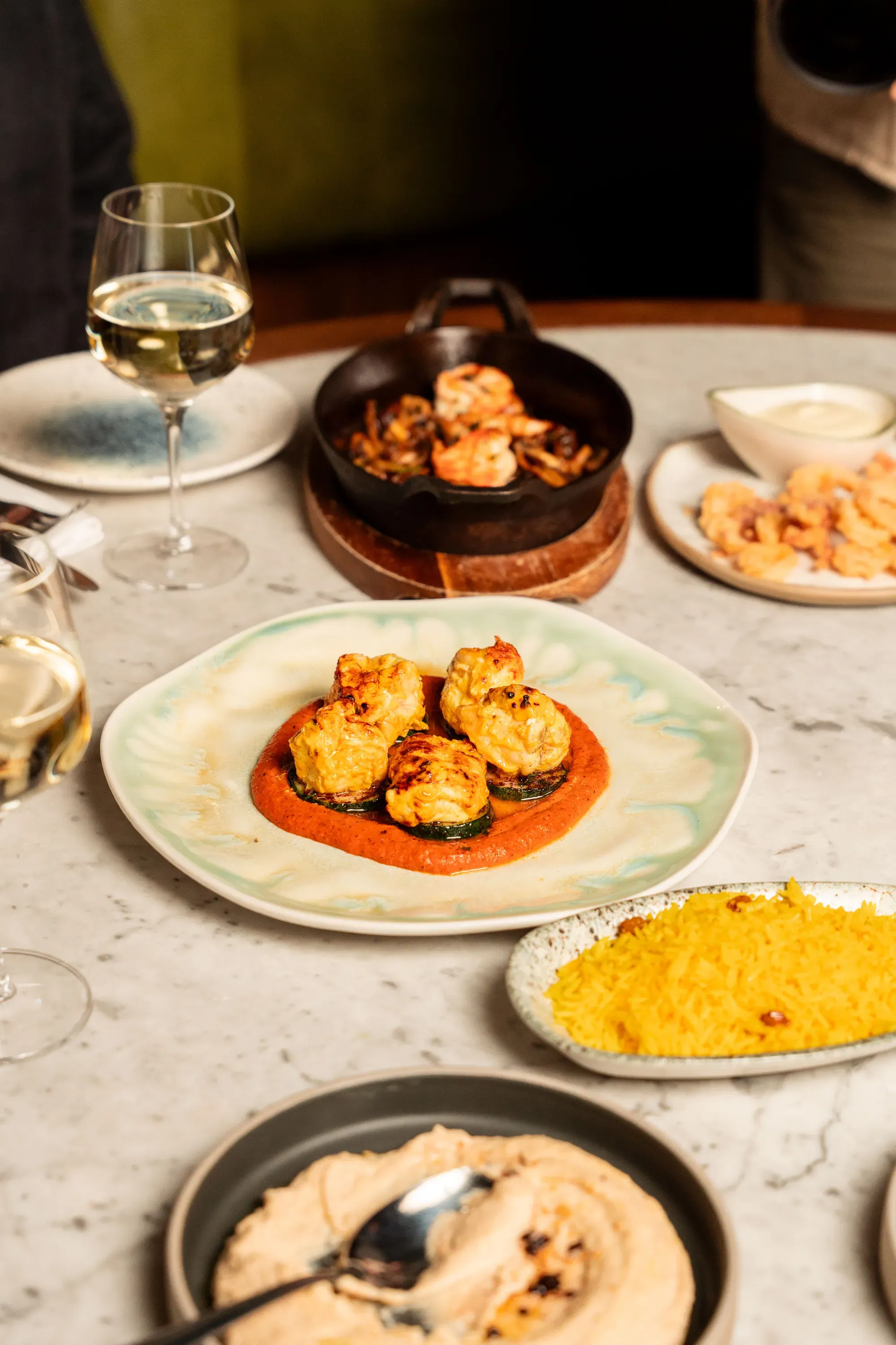 Grilled prawns on romesco sauce with hummus, saffron rice and white wine on a marble table
