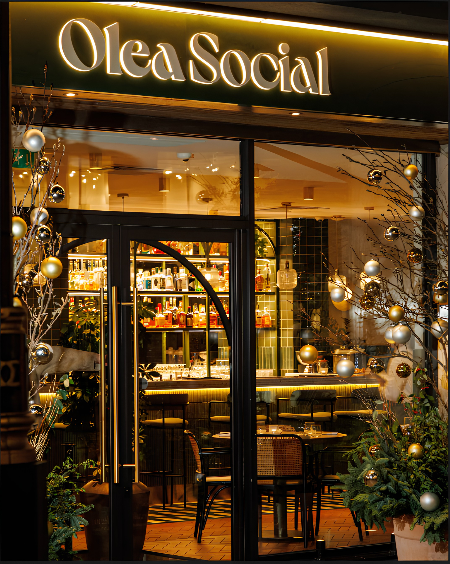 Olea Social shopfront at night, lit sign and windows decorated with gold and silver baubles